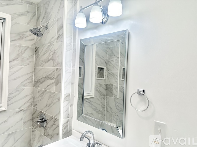 A bathroom with a marble tile shower and a rectangular mirror.
