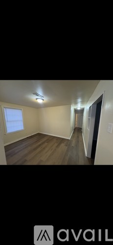 A room with wooden flooring and a window on the left side.