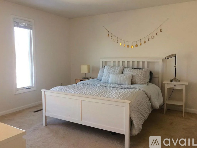 A bedroom with a white bed and a string of lights above it.