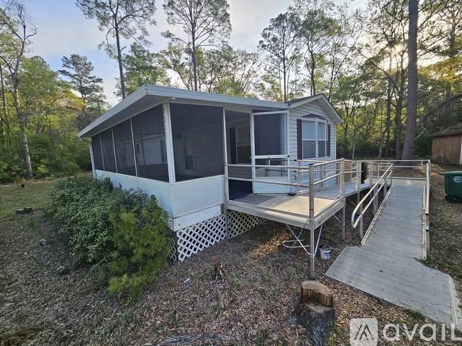 A house with a deck and a screened porch is surrounded by trees.