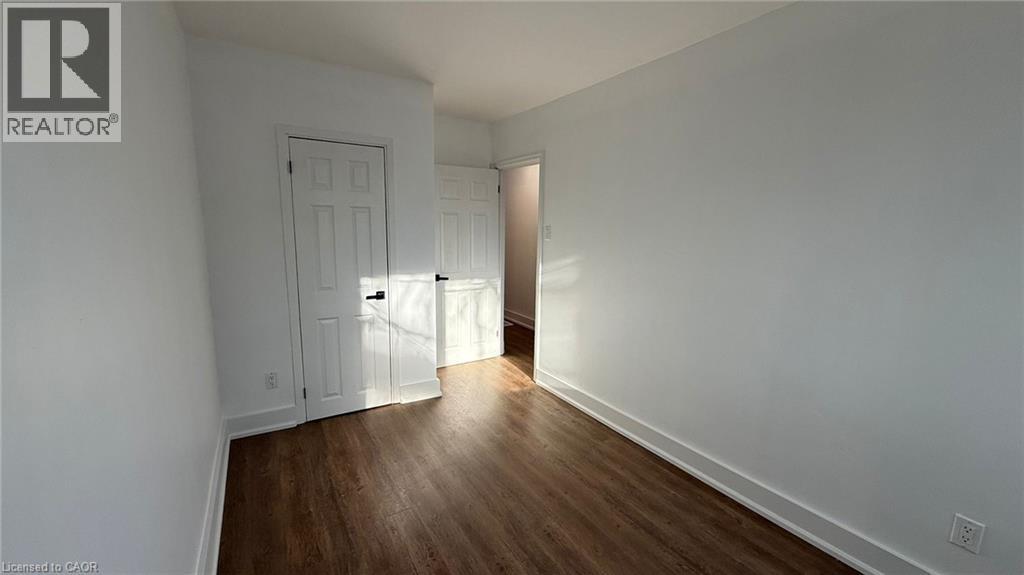 A room with a wooden floor and white walls, with a door on the left and a doorway on the right.