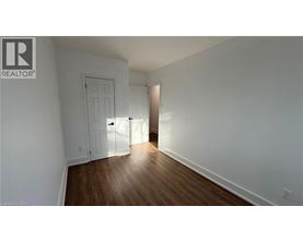 A room with a wooden floor and white walls, with a door on the left and a doorway on the right.