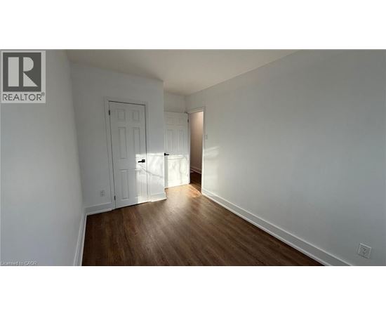 A room with a wooden floor and white walls, with a door on the left and a doorway on the right.