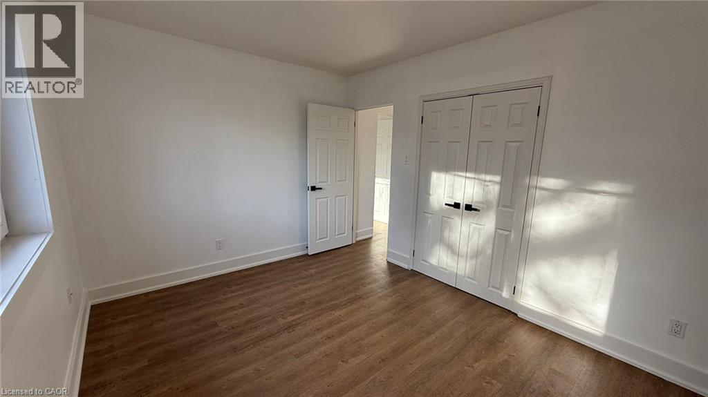 A room with wooden floors and white walls, with a door on the right and a window on the left.