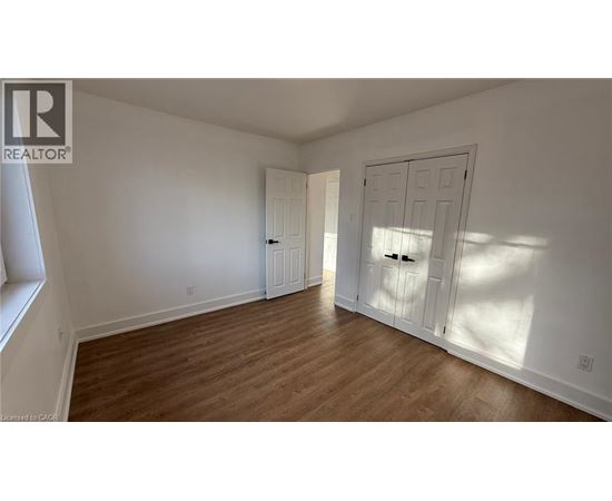A room with wooden floors and white walls, with a door on the right and a window on the left.