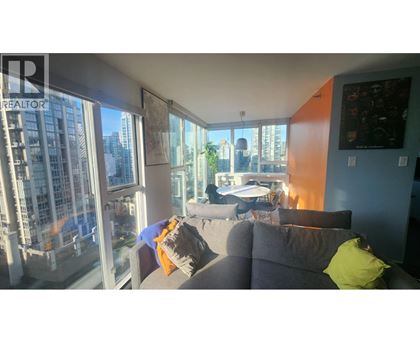 A living room with a grey couch and a large window overlooking a cityscape.