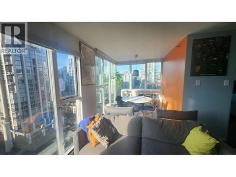 A living room with a grey couch and a large window overlooking a cityscape.