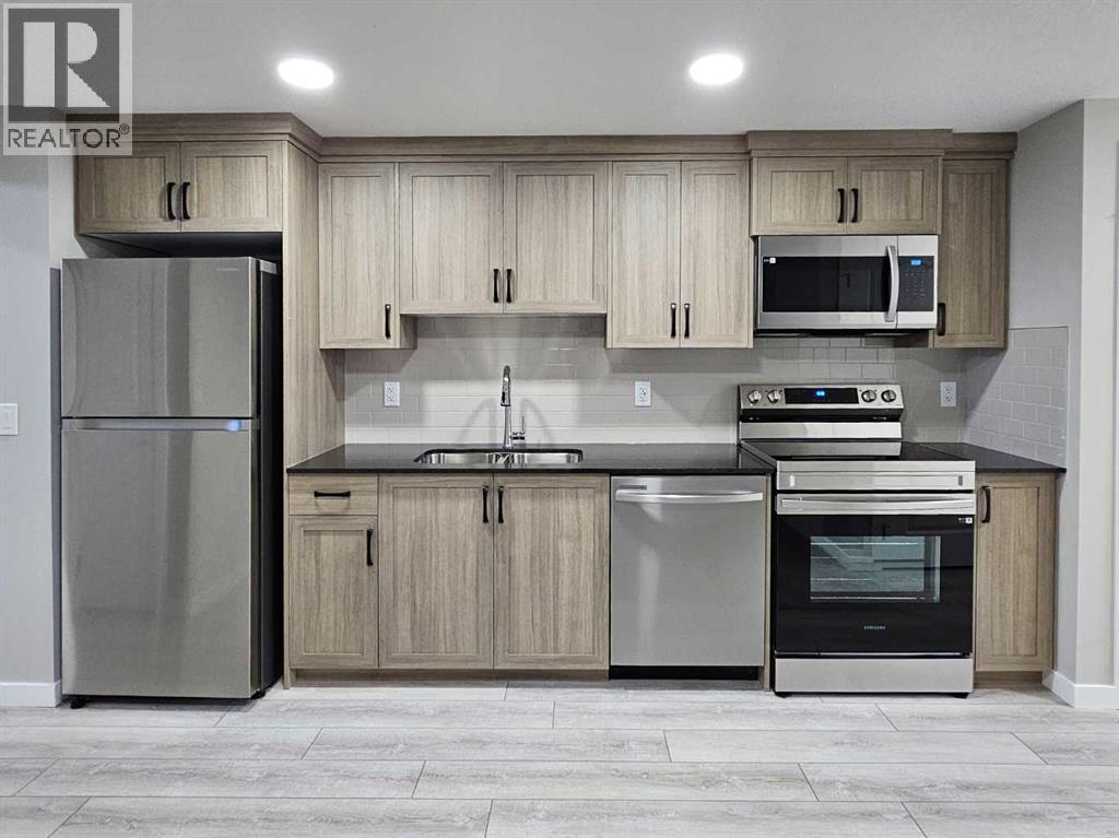 A kitchen with a refrigerator, microwave, oven, and sink.
