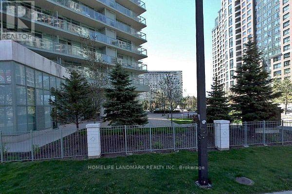 A tall building with a glass facade is surrounded by a metal fence and trees.