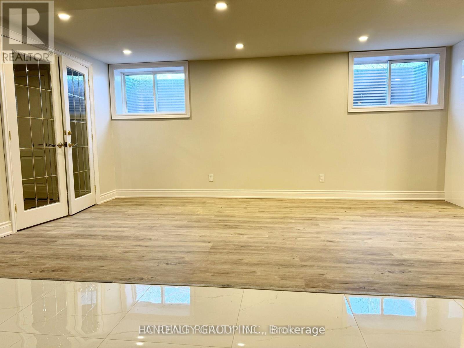 A spacious room with wooden flooring and two windows.