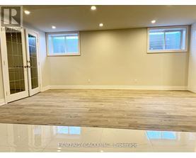 A spacious room with wooden flooring and two windows.