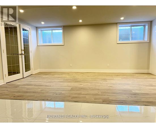A spacious room with wooden flooring and two windows.