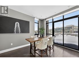A dining room with a wooden table and chairs, a large window, and a painting on the wall.