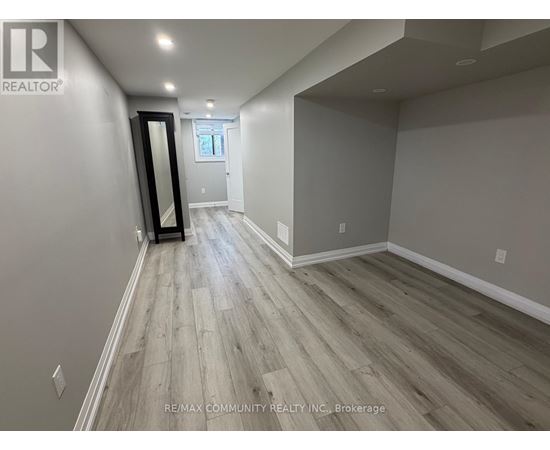 A spacious room with wood flooring and a large mirror on the wall.