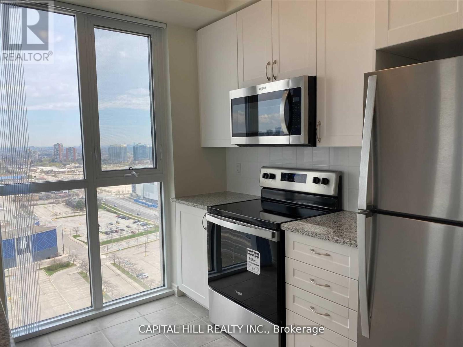 A kitchen with a stainless steel refrigerator, a microwave above the stove, and a view of the city from the window.
