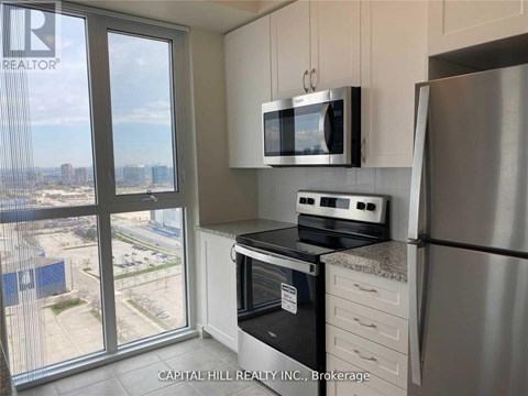 A kitchen with a stainless steel refrigerator, a microwave above the stove, and a view of the city from the window.