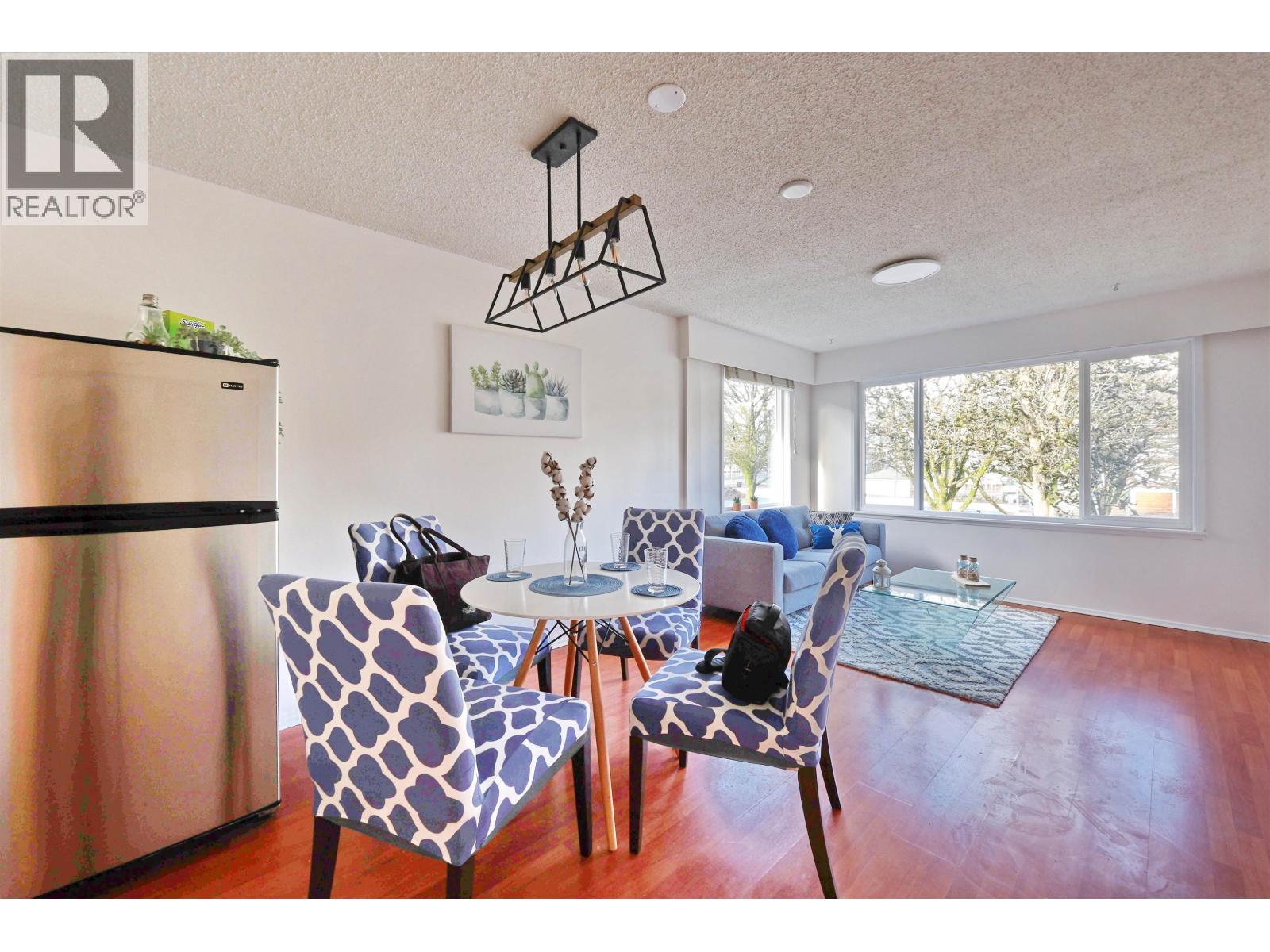 A modern dining room with a stainless steel refrigerator and a glass table.