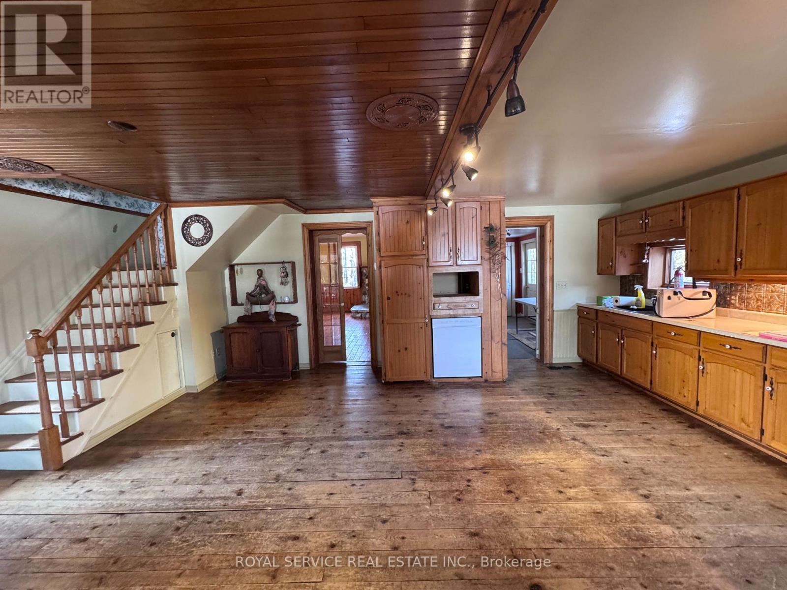 A spacious room with wooden floors and a staircase on the left side.