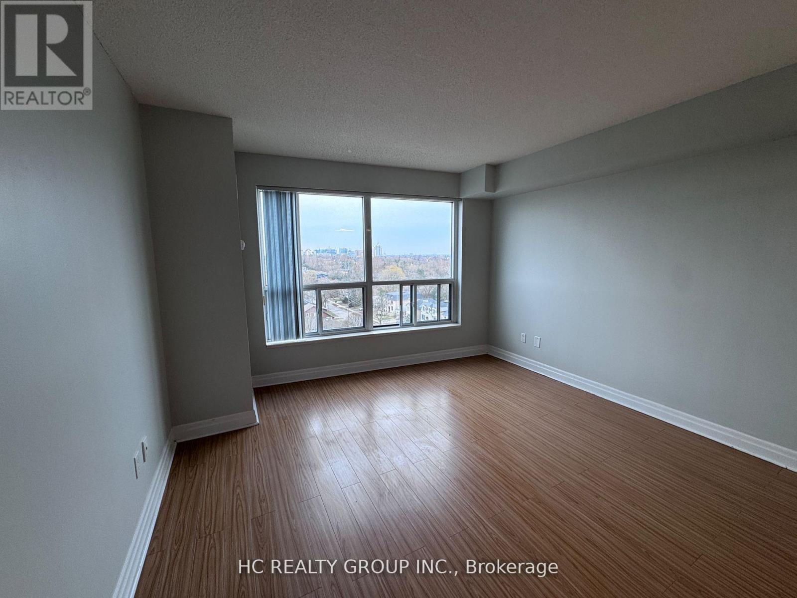 A room with wooden flooring and a large window overlooking a cityscape.