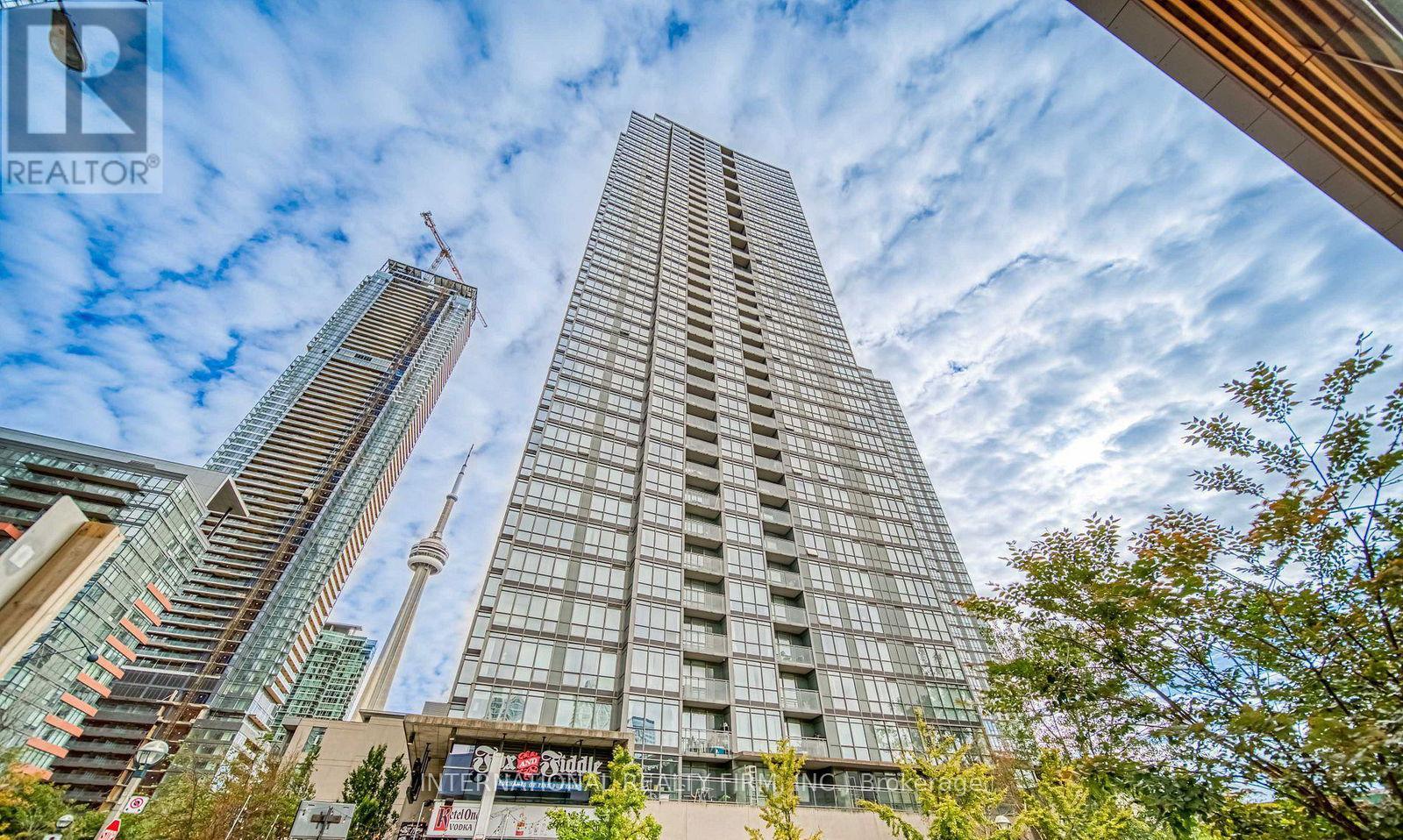 A tall building with a glass facade stands in front of a skyline with other skyscrapers.