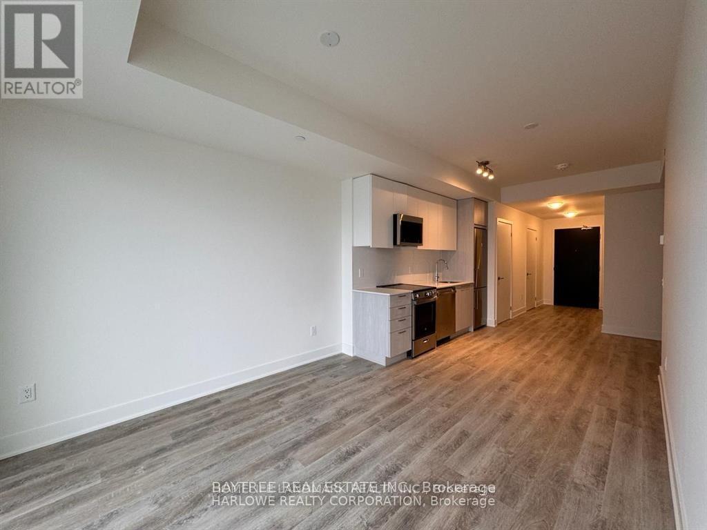 A spacious living room with wood flooring and a kitchen area in the background.