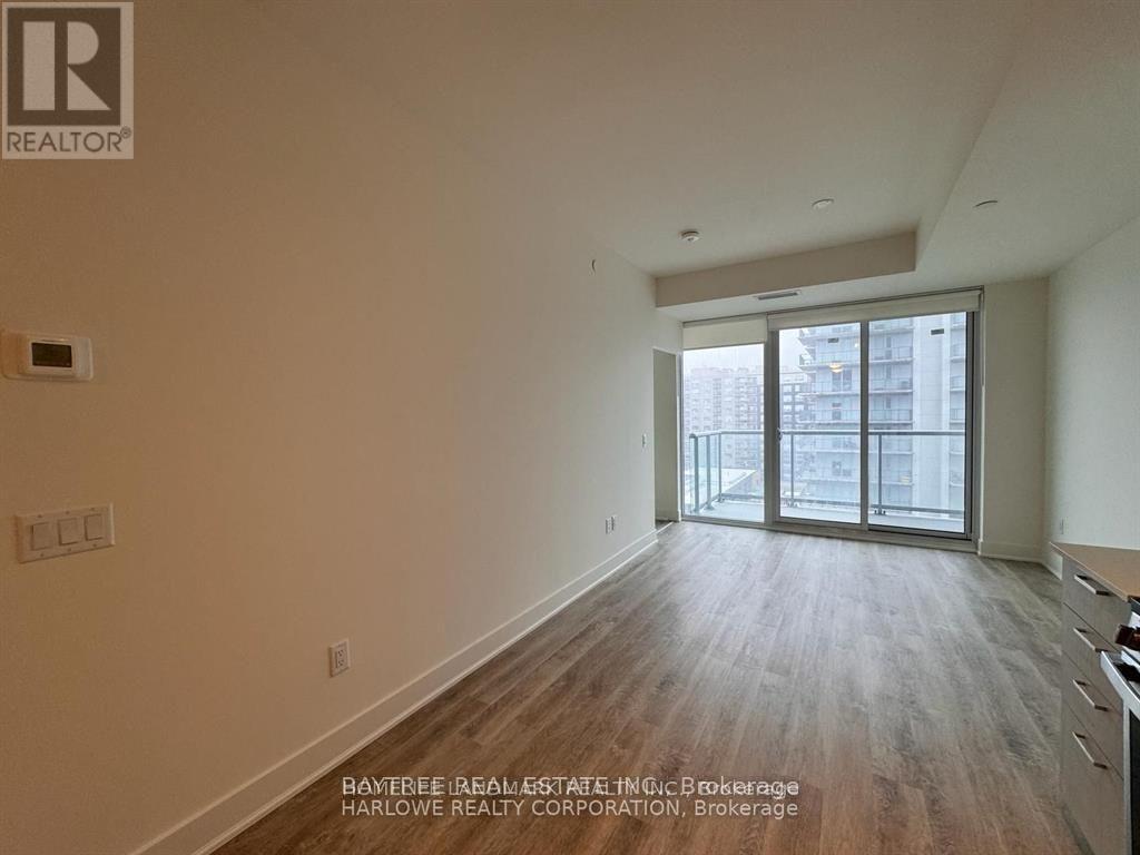 A spacious room with wooden flooring and a large window.