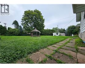 A gazebo sits in a grassy backyard with a house in the background.