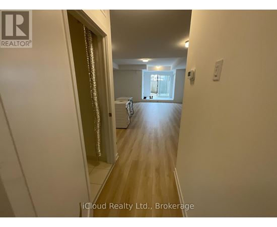 A hallway with a door on the left and a bedroom with a bed and a window on the right.