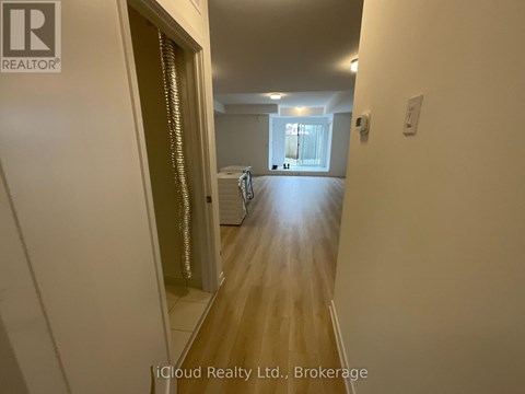 A hallway with a door on the left and a bedroom with a bed and a window on the right.