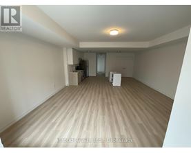 A spacious room with wooden flooring and a refrigerator in the corner.