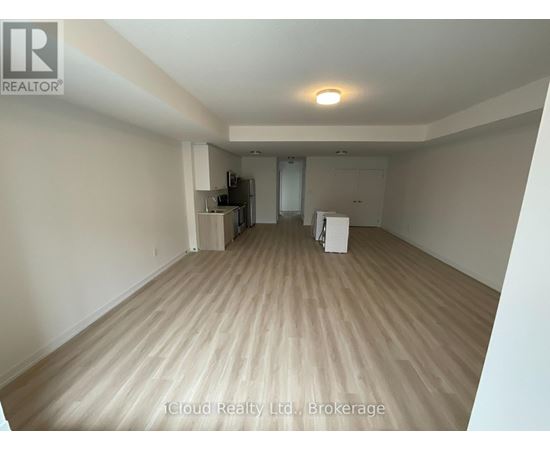 A spacious room with wooden flooring and a refrigerator in the corner.