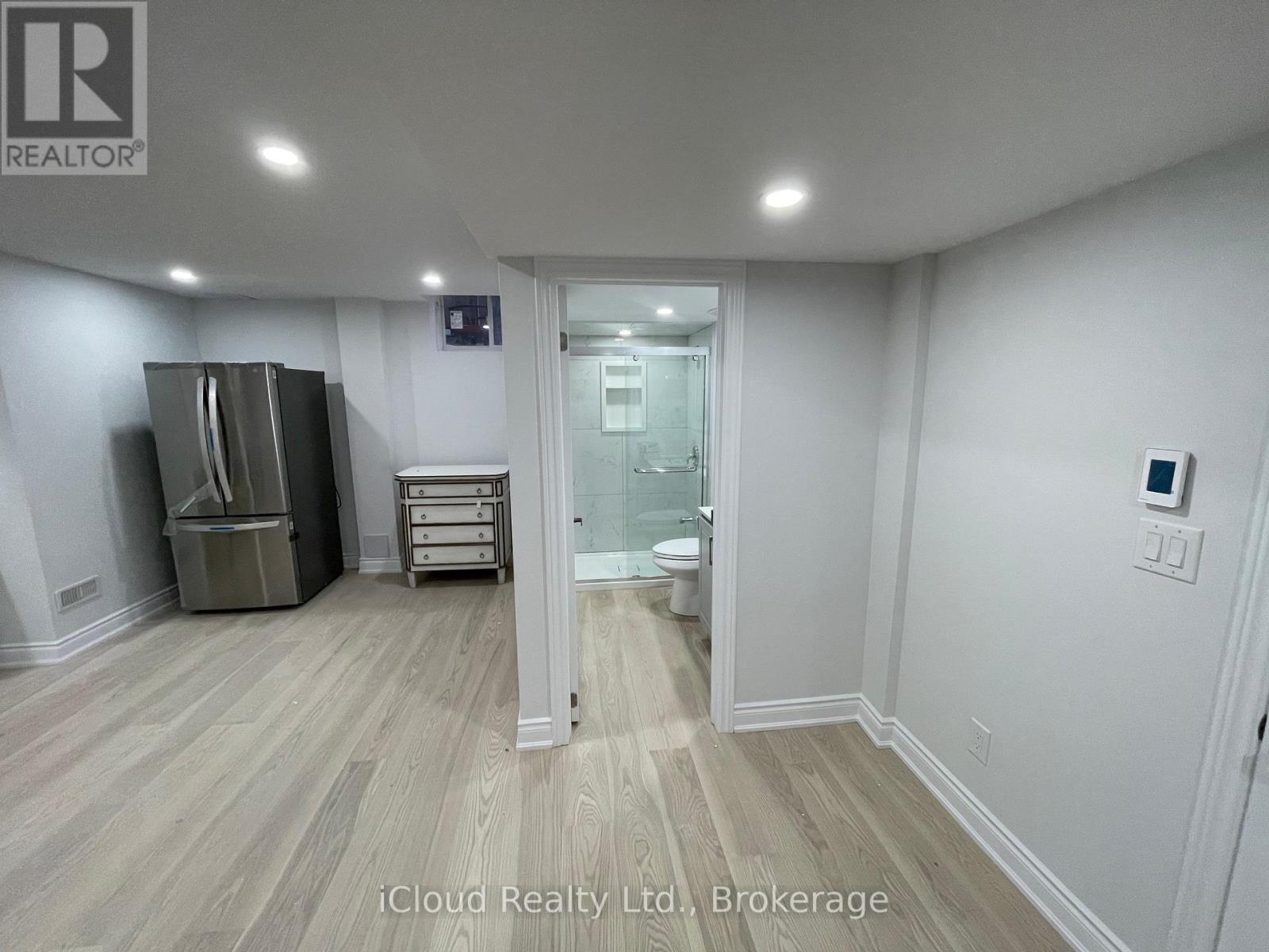 A room with a wooden floor and white walls, with a doorway leading to another room.