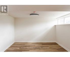 A room with a wooden floor and a smoke detector on the ceiling.