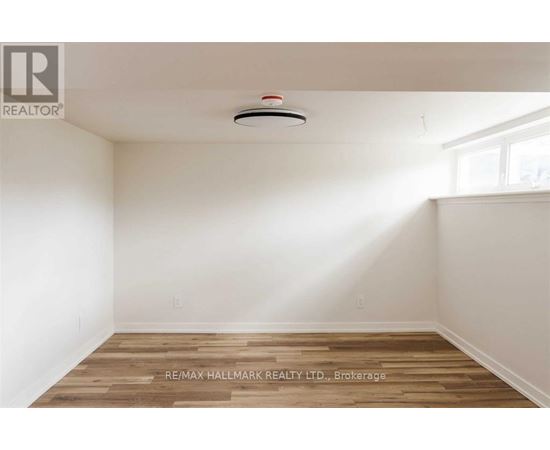 A room with a wooden floor and a smoke detector on the ceiling.