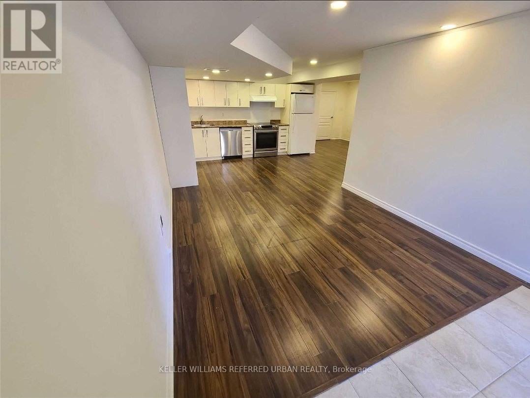 A spacious room with wooden flooring and a kitchen area in the background.