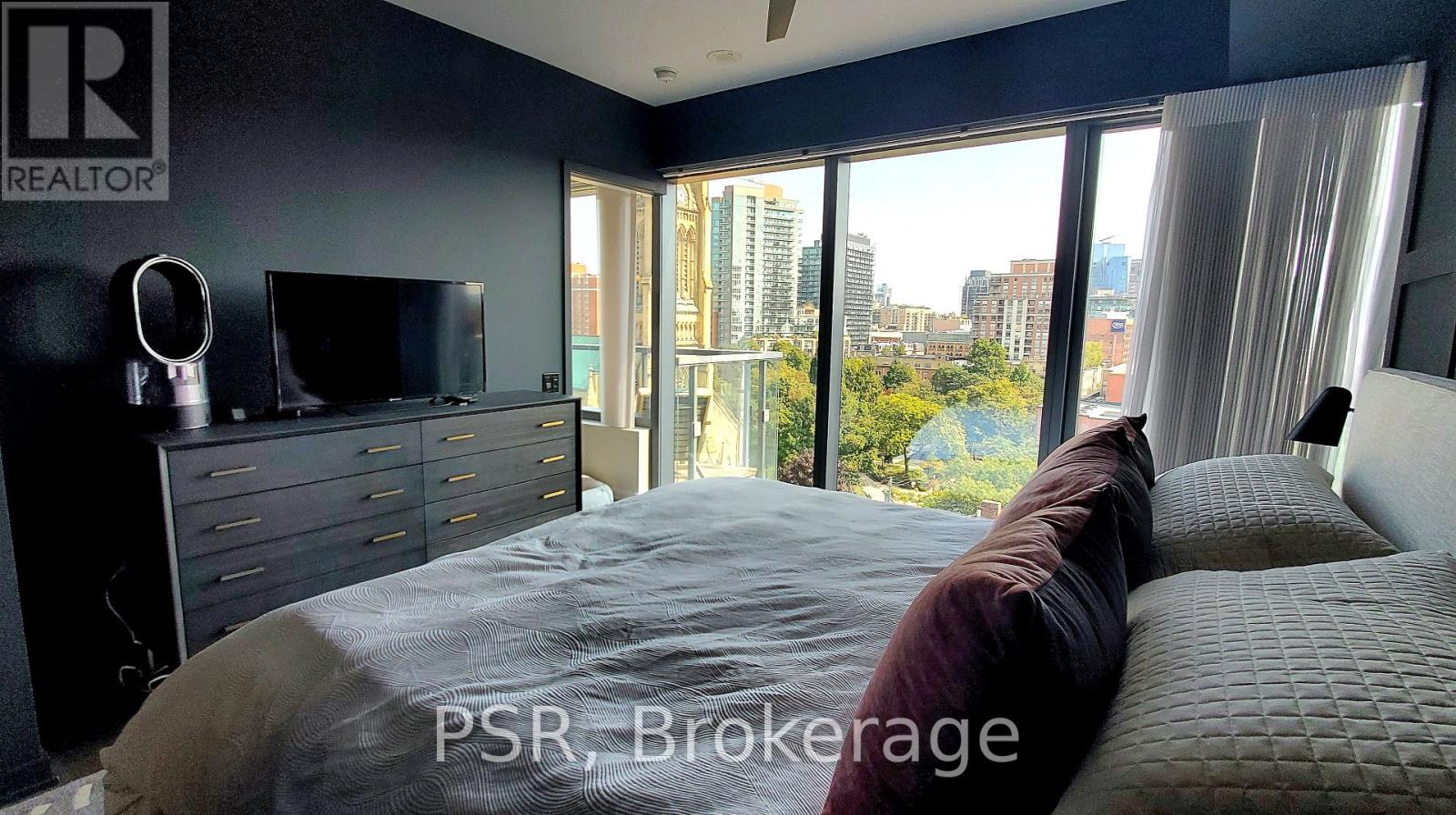A bedroom with a large bed and a city view through the window.