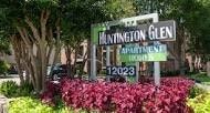 A green sign for Huntington Glen Apartments is in front of some trees and flowers.