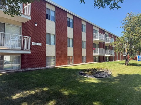 A red brick apartment building with balconies and a green lawn in front.