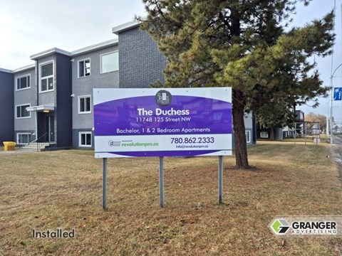 A sign for The Duchess apartment complex is installed in front of a building.
