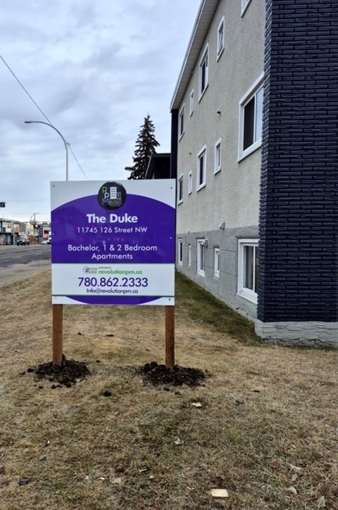 A sign for The Duke apartment complex is in front of a building.