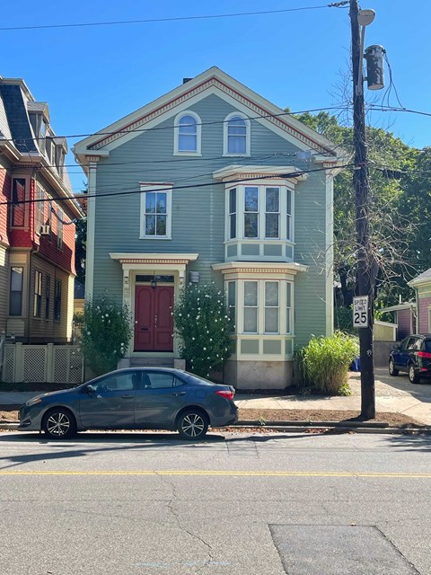 A blue house with a red door is on the corner of a street.
