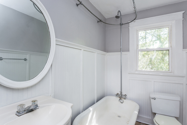 A white bathroom with a round mirror, sink, toilet and bathtub.