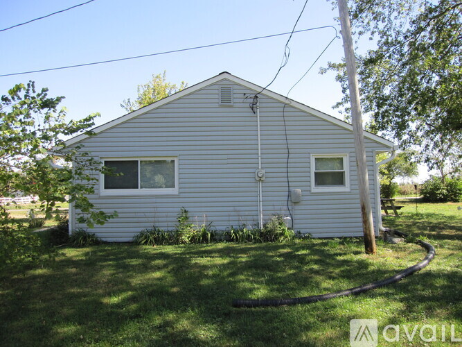 A house with a grey siding and a white window is surrounded by green grass.