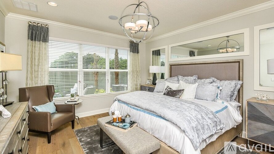 A well-lit bedroom with a large bed and a chair.