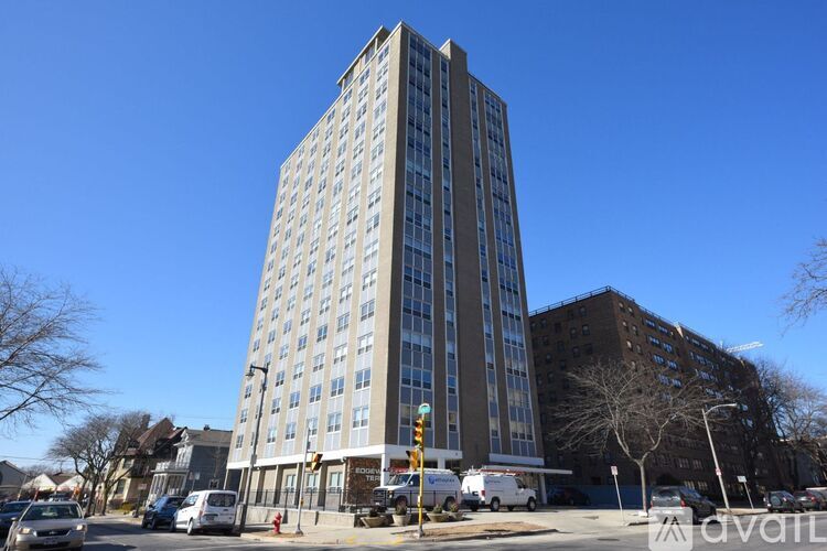 A tall building with many windows is in the middle of a street with cars and trees.