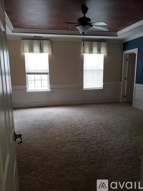 A room with a carpeted floor, a ceiling fan, and two windows with blinds.