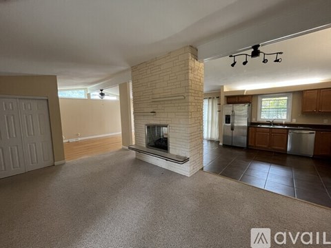 A living room with a fireplace and a kitchen area in the background.