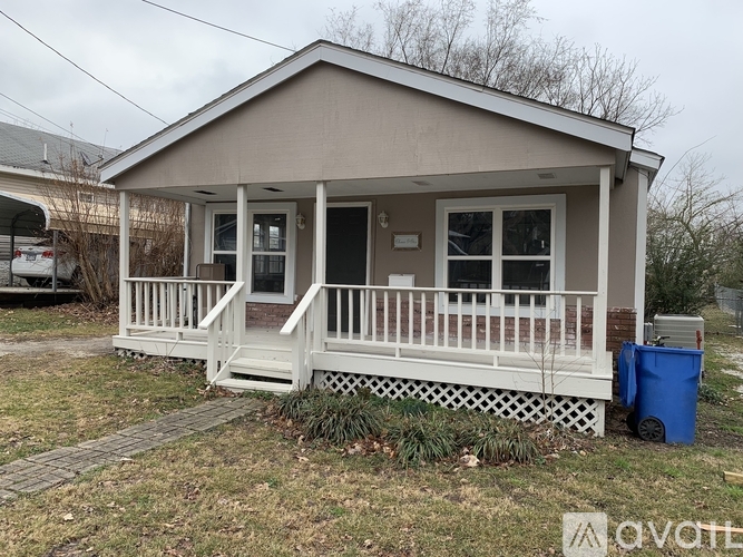 A small house with a porch and a trash can in front.