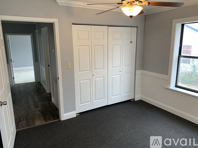 A room with a white door, a ceiling fan, and a window.