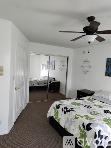 A bedroom with a bed, a ceiling fan, and a mirror.